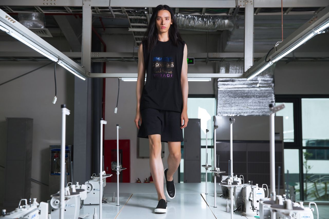 Model walking confidently on a runway in an industrial environment, showcasing casual fashion.